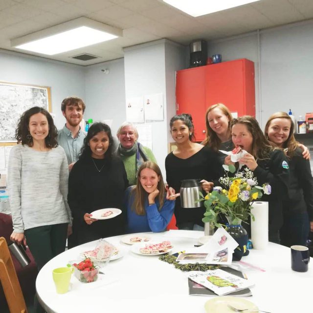 Students, staff, and faculty gather around a table for tea, treats. 